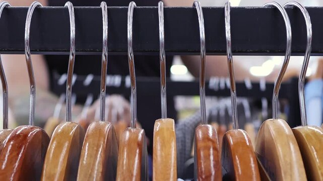 Man Choosing Shirts Behind Wooden Hangers in Department Store. Customer browses clothing through rack. Concept of mens fashion, retail shopping, consumer choice and apparel selection.