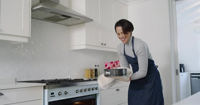 Three adult women watching woman in dark apron lifting springform pan from oven, smiling at counter
