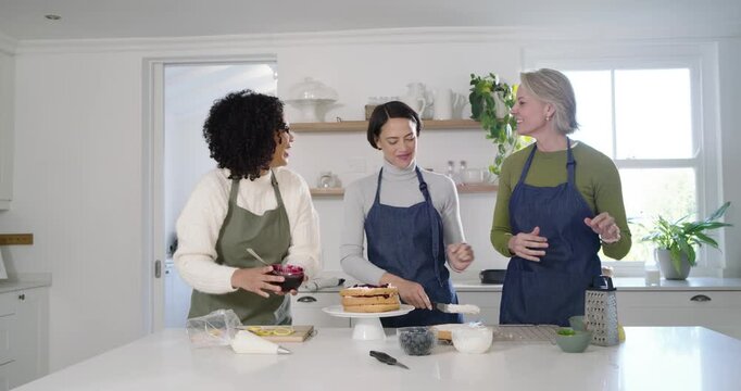 Diverse women assembling cake in kitchen left scooping compote center spreading right passing tools