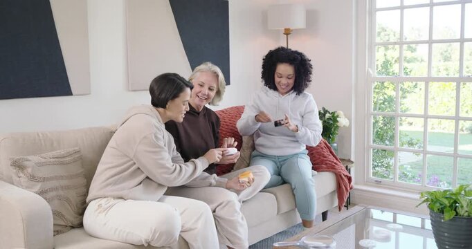 Diverse female friends testing skincare on sofa, left woman handing jar starting passing pads