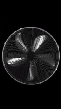 Metallic fan spins against a black background in vertical video. Blurred blades rotate behind a circular protective grille.