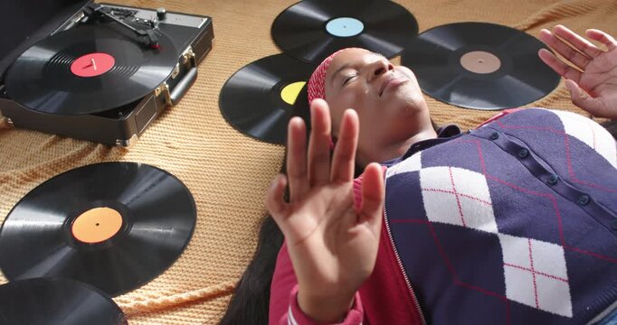 African American woman lying on blanket in argyle vest, reacting to turntable playing vinyl smiling