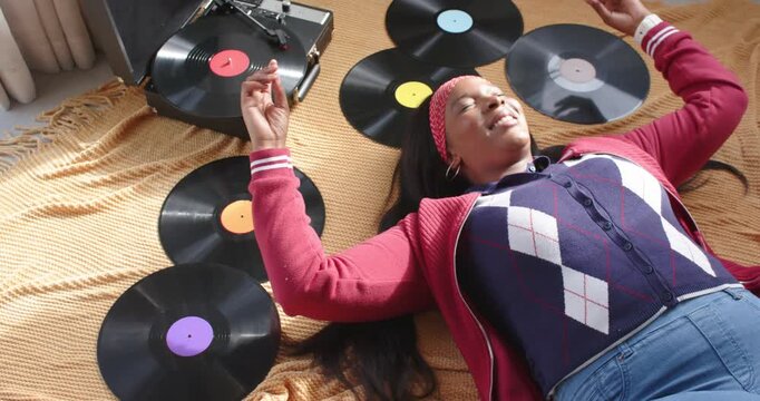 African American woman lying on blanket on floor, listening to vinyl on turntable, moving hands