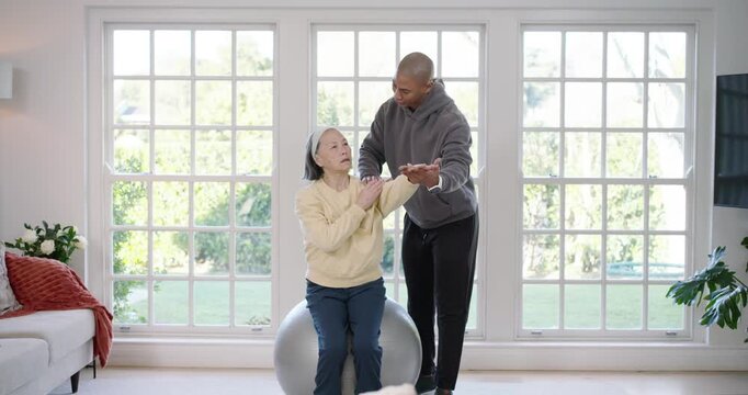 Senior woman sitting on exercise ball, therapist placing hand on shoulder, guiding arm mobility