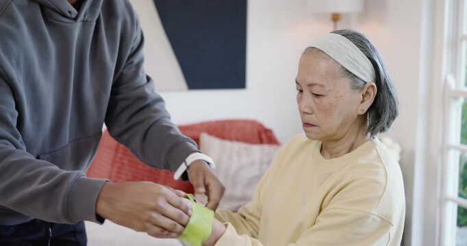 African American man placing green band on Senior Asian woman on sofa, guiding stretch, copy space