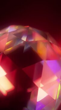 Colorful reflections move across faceted glass in vertical video. Warm multicolored facets create an abstract geometric texture.