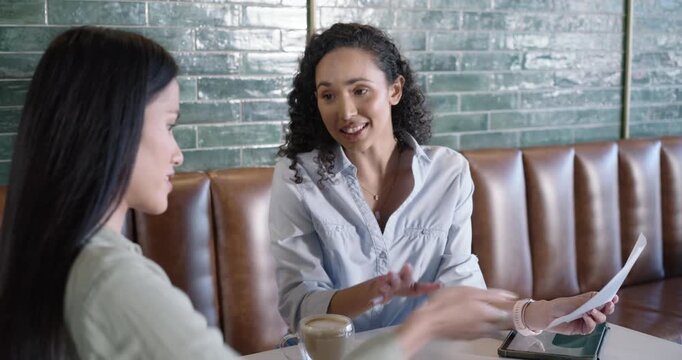 African American woman showing paper and explaining project to Asian woman at coffee booth