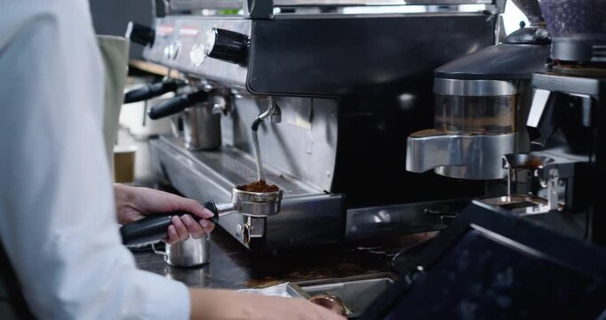 Female barista reaching for grinder, dosing, tamping, pulling into to-go cups at cafe, copy space