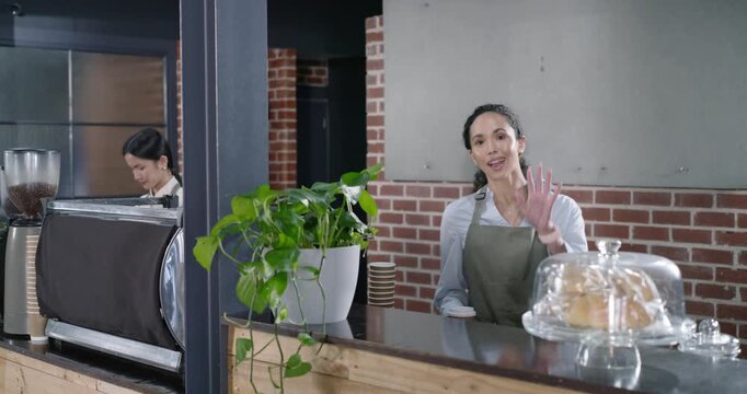 Diverse staff, camera closing in, green-apron barista placing two to-go cups at counter for pickup