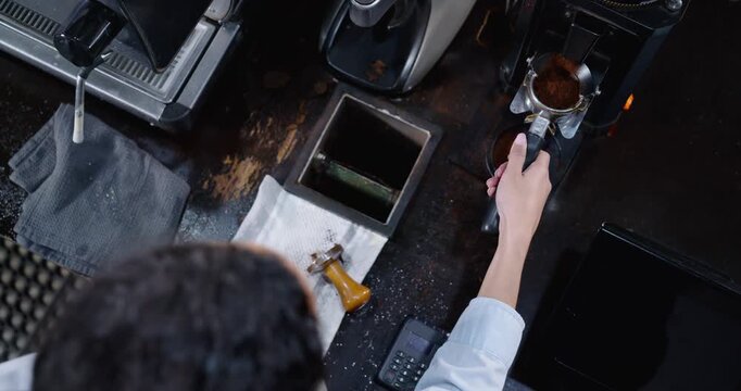 Barista is starting grinder, tamping portafilter, extracting espresso at cafe counter for order