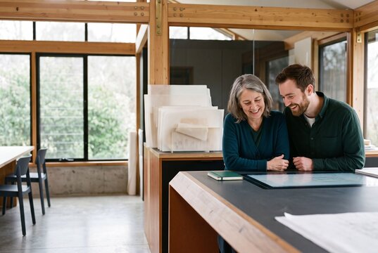 Two smiling architects collaborating over blueprints at a desk in a modern design studio