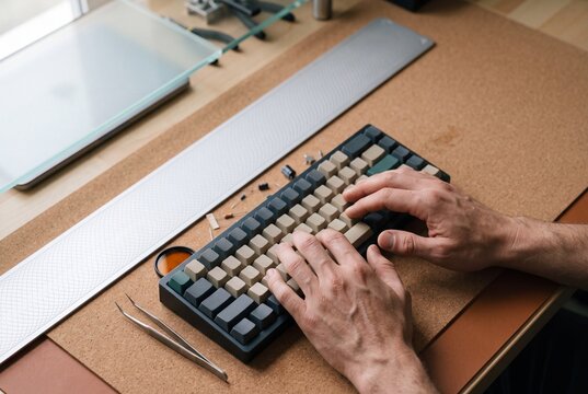Male hands typing on a custom mechanical keyboard placed on a cork desk mat in a workshop setting