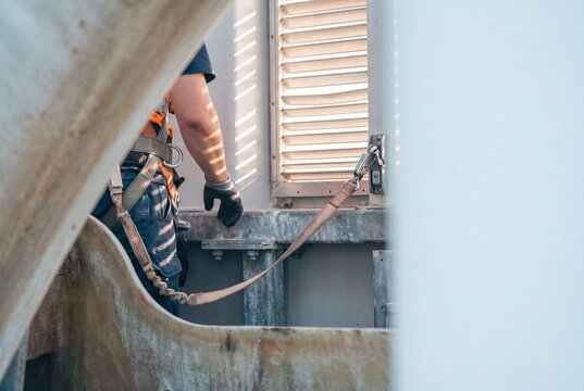 Industrial technician wearing fall protection safety harness anchored to an anchor point on a high structure