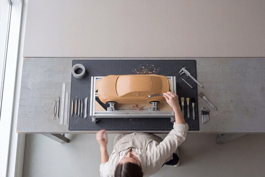 Top view of a female automotive designer sculpting a prototype clay car model at a studio workbench