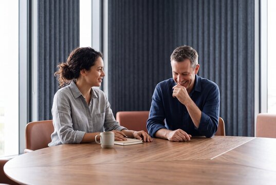 Two diverse colleagues talking and laughing together during a casual business meeting in a modern conference room