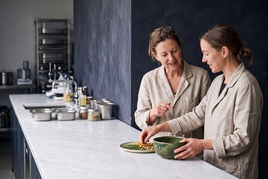 Two female chefs in professional uniform preparing healthy organic ingredients on a marble counter in a modern kitchen