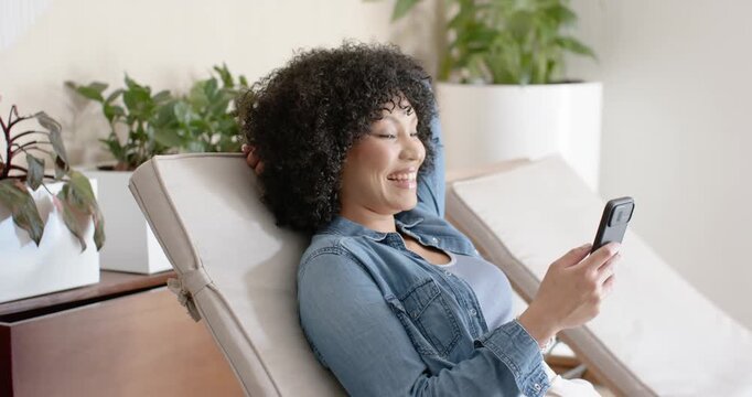 African American woman reclining in lounge in denim jacket, reading message and scrolling phone