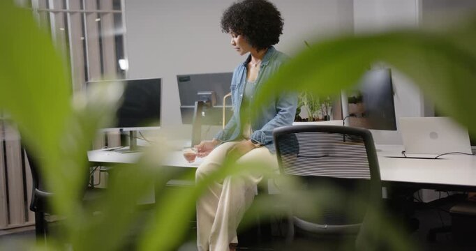 African American woman shifting while sitting desk lifting mug, sipping and reflecting at office