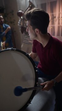 Vertical shot of multiethnic young adult male football fans playing brass instruments and bass drum at home. Ideal for sports fandom campaigns and victory promos