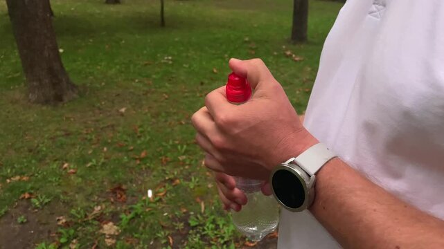 Close-up of a man using a red spray bottle in a park, personal care and active lifestyle, healthy routine, outdoor recreation.