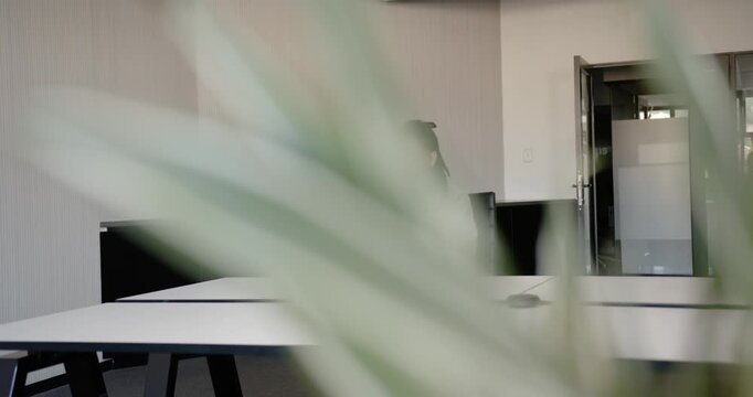 Nonbinary African American adult working on laptop in office as plant swaying revealing speaker