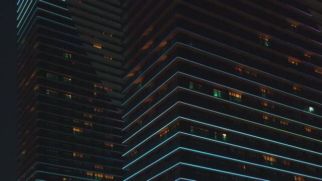 Night view of modern residential high-rise skyscrapers featuring dynamic blue LED contour illumination flashing and moving along balconies and building edges.