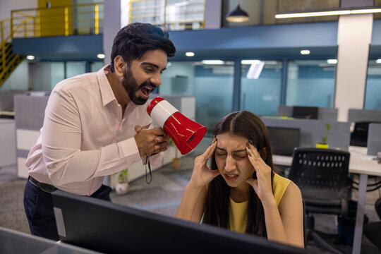 Indian angry businessman shouting at employee woman holding megaphone standing in modern office. professional communication problem sitting at the desk who does not want to work