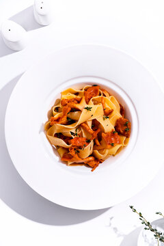 Homemade pasta with chanterelles and fresh thyme garnish on white plate. Italian food dish rich in wild mushrooms and carbohydrates. Authentic vegetarian cuisine, healthy eating recipe.