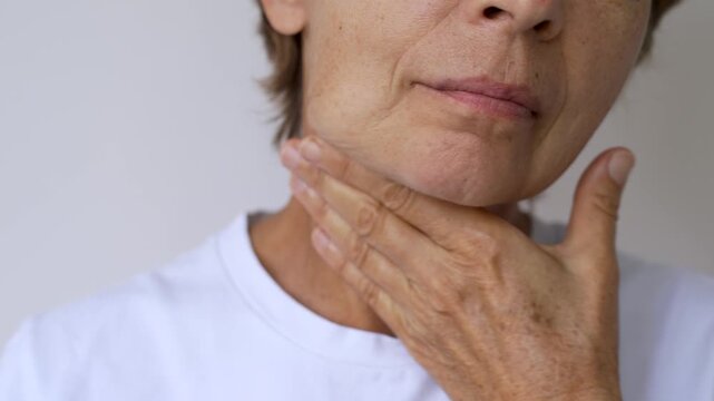 Mature woman touches the skin under her chin and near the neck, showing sagging skin, wrinkles, age spots and natural signs of aging