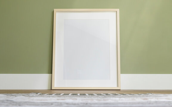 Blank vertical photo frame mockup standing on floor against olive green wall - photography
