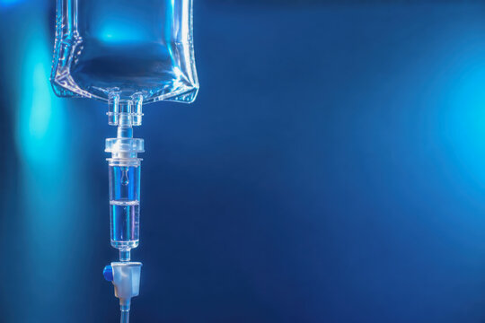 IV drip chamber close up with saline fluid dripping on blue background