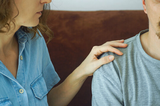 Woman sitting on sofa while touching man's shoulder, close-up. Portrays empathetic listening, supportive partnership, and nonverbal validation during difficult conversations between romantic partners.