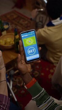 Vertical video of African American young adult holding smartphone with online sports betting app among cheering friends. Perfect for sportsbook and digital gaming promotions