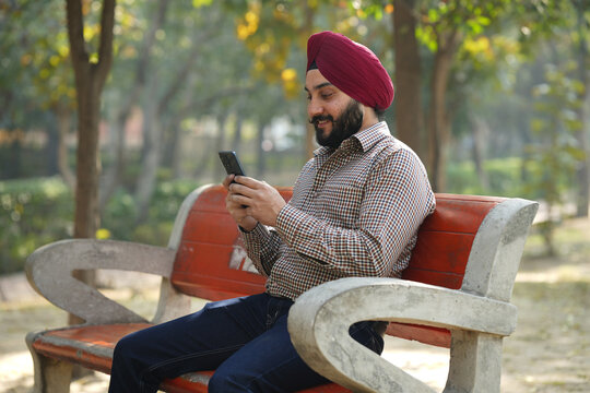 Happy Indian young sikh man using a mobile phone at park Outdoors