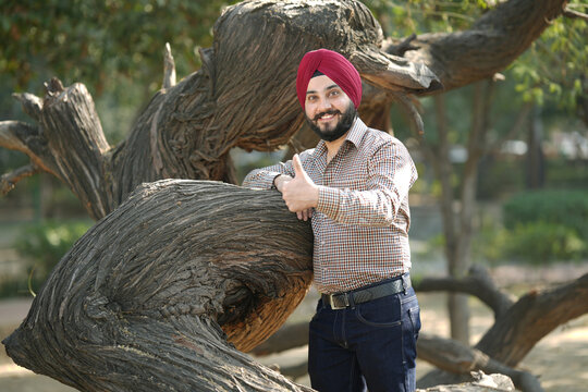 Indian happy sikh man showing thumbs up while sitting on bench at park.