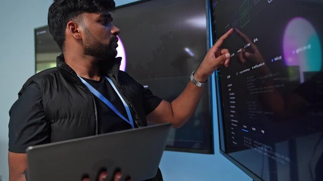 Programmer presenting code solutions in a modern tech environment with multiple screens and a laptop