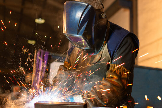 Close up of industrial welder wearing helmet while welding with sparks
