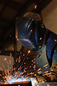 Vertical close up of industrial welder welding with protective helmet and sparks