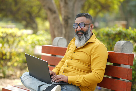 Portrait od cheerful smiling indian senior man working on laptop in garden. Happy Elderly white-haired people smiling carefree, old Bearded male with positive emotion. all good expression.