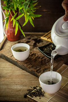 A hand pouring hot organic oolong tea from a ceramic teapot into a white cup on a rustic wooden table. Traditional Asian tea ceremony concept for wellness, mindfulness, and healthy lifestyle.