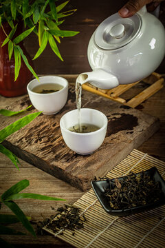 A hand pouring hot organic oolong tea from a ceramic teapot into a white cup on a rustic wooden table. Traditional Asian tea ceremony concept for wellness, mindfulness, and healthy lifestyle.