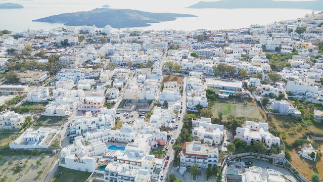 Aerial view of Santorini showcasing whitewashed buildings, blue domes, and lush greenery with the Aegean Sea and volcanic islands in the background under a clear sky