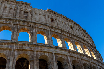 Fototapeta premium Famous Coliseum in Rome. Colosseum, or Coliseum. Part of the wall of an antique stone structure with arches. Italy, Europe. Famous touristic place in the world, Europe. Beautiful blue sky background.