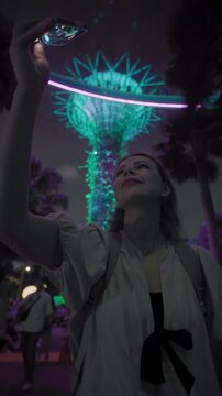Visitor filming bright tree light show on mobile phone at Gardens by the Bay Singapore showcasing night city beauty and tourism in Asia