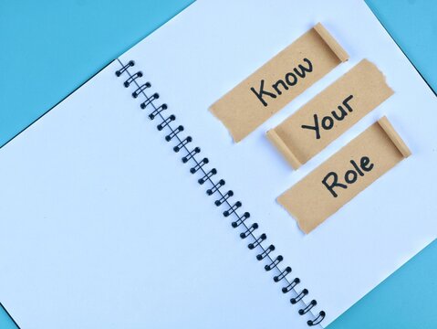 Know Your Role text handwritten on torn brown paper strips over an open book page with blue background. Business concept for responsibility, clarity, teamwork, and job duties