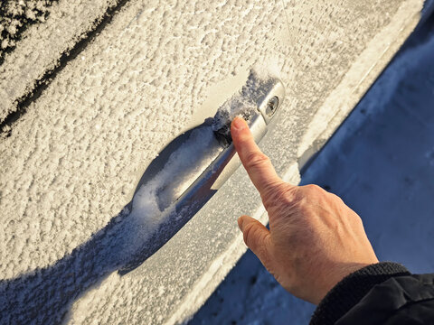 Frozen car door lock is covered in snow and ice in a cold winter setting while trying to open the vehicle