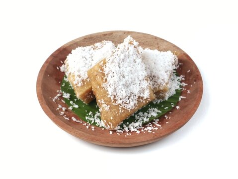 Uli singkong or traditional indonesian steamed cassava cake topped with freshly grated coconut served on a banana leaf and wooden plate, isolated on a white background. Delicious sweet authentic snack