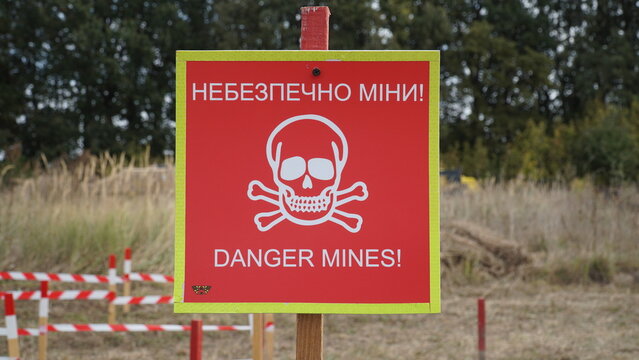 Red danger mines warning sign with skull and crossbones in a field in Ukraine. Landmine danger sign in Ukrainian and English language.