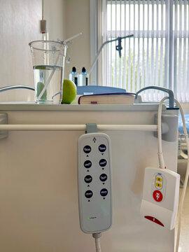 Hospital room bedside table with remote control handsets, emergency call button, glass of water and green apple for patient care and rehabilitation