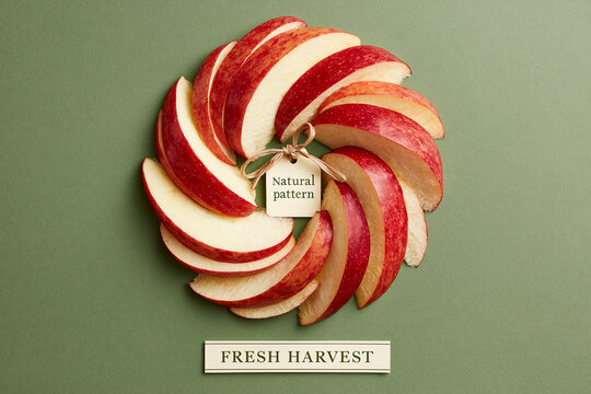 Sliced fresh red apple arranged in a circular pattern on a green background with 'Fresh Harvest' label.